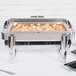 A Vollrath stainless steel roll top chafer on a table with food in it.