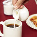 A person pouring white creamer into a white cup of coffee.