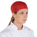 A chef wearing a red Headsweats chef cap on a counter in a professional kitchen.