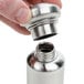 A hand holding a stainless steel American Metalcraft salt and pepper shaker set.