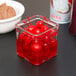 An American Metalcraft square glass condiment jar with red liquid and cherries in it.