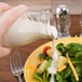 A person pouring white sauce onto a salad.