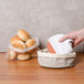 A hand holding a white towel in a round bread basket with rolls.