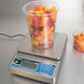 An Edlund waterproof digital portion scale with a plastic cup full of fruit on it.