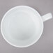 An Arcoroc white porcelain cup with a handle on a gray surface.