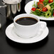 An Arcoroc white porcelain stackable coffee cup on a plate with a salad.