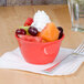 A red Thunder Group melamine bowl filled with fruit and a fork.
