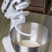 A white KitchenAid stand mixer with a dough hook and a bowl of dough in it.