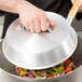 A hand holding a Town aluminum wok cover over a wok of food.