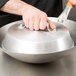 A hand holding a Town aluminum wok cover over a wok.