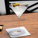 A Stolzle martini glass with a drink and olives on a table.