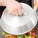 A person holding a Town aluminum wok lid over vegetables cooking in a wok.