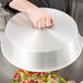 A person holding a Town aluminum wok cover over a bowl of vegetables.