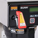A Bunn Axiom DV-TC coffee brewer on a hospital cafeteria counter with a red and yellow sticker.