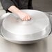 A hand holding a Town aluminum wok cover over a large metal pan.