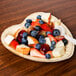A white Eco-gecko heart shaped palm leaf plate filled with fruit on a table.