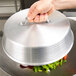 A hand holding a Town aluminum wok cover over a bowl of vegetables.