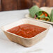 A white table with a bowl of red sauce in a brown Eco-gecko palm leaf bowl and green vegetable wraps.
