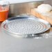 An American Metalcraft heavy weight aluminum pizza pan with perforations on a counter next to a bowl of dough.