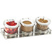 A Cal-Mil stainless steel horizontal display with three hinged glass jars filled with nuts and berries on a counter.