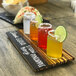 A Cal-Mil Crushed Bamboo flight tray with drinks and lime wedges on a wood board.