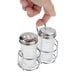 A hand holding a stainless steel condiment caddy with salt and pepper shakers.