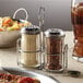 A stainless steel condiment caddy with salt and pepper shakers on a table.