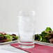 A close up of an Arcoroc beverage glass full of clear liquid with ice on a plate of salad.