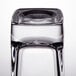 A close up of a clear Arcoroc tall square shot glass with a black rim on a table.