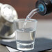 A glass of water being poured into an Arcoroc shot glass.