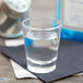 An Arcoroc shot glass filled with clear liquid on a napkin.