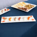 A Tablecraft white rectangular melamine tray with appetizers and crackers on a table.