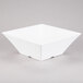 A white square Tablecraft melamine bowl with a corner on a gray surface.