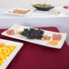 A Tablecraft white rectangular melamine tray on a table with plates of food and fruit.