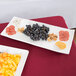 A Tablecraft white rectangular melamine tray with fruit and cheese on a table.