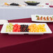 A Tablecraft white melamine tray with fruit and canapes on a table.