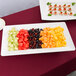 A Tablecraft white rectangular melamine tray with fruit and canapes on a table.