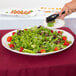A Tablecraft white round pebbled melamine tray with salad being served on it.