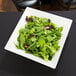 A white square Tablecraft melamine bowl filled with salad on a table.