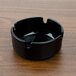 An Arcoroc black glass ashtray on a wood surface.