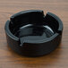 An Arcoroc black round glass ashtray on a wood surface.