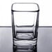 A clear Arcoroc square shot glass on a table with a reflection.