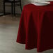 A table with a burgundy Intedge round tablecloth and a white plate on it.