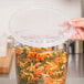 A hand holding a Cambro translucent plastic container filled with pasta with a plastic lid on top.