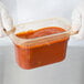 A person in white gloves holding a Carlisle plastic container of red sauce.