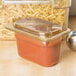 A Carlisle amber plastic food pan with pasta and sauce in it on a counter with a lid.