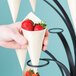 A hand holding strawberries in a black cone.