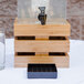 A bamboo crate beverage dispenser with an ice chamber sitting on a table with a glass of water.