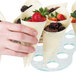 A hand holding a wooden serving cone filled with strawberries and berries.