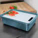 A blue HS Inc. cutting board in a blue container with white liquid and diced tomatoes on a counter.